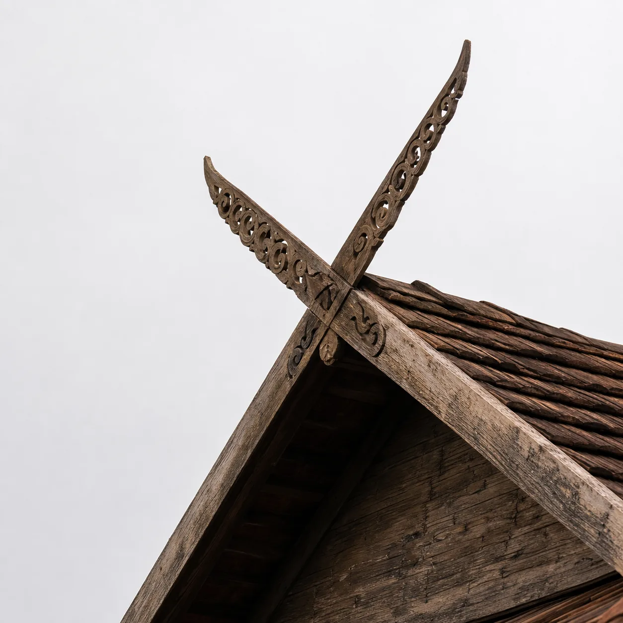Crossed kalae roof finials against an overcast white sky