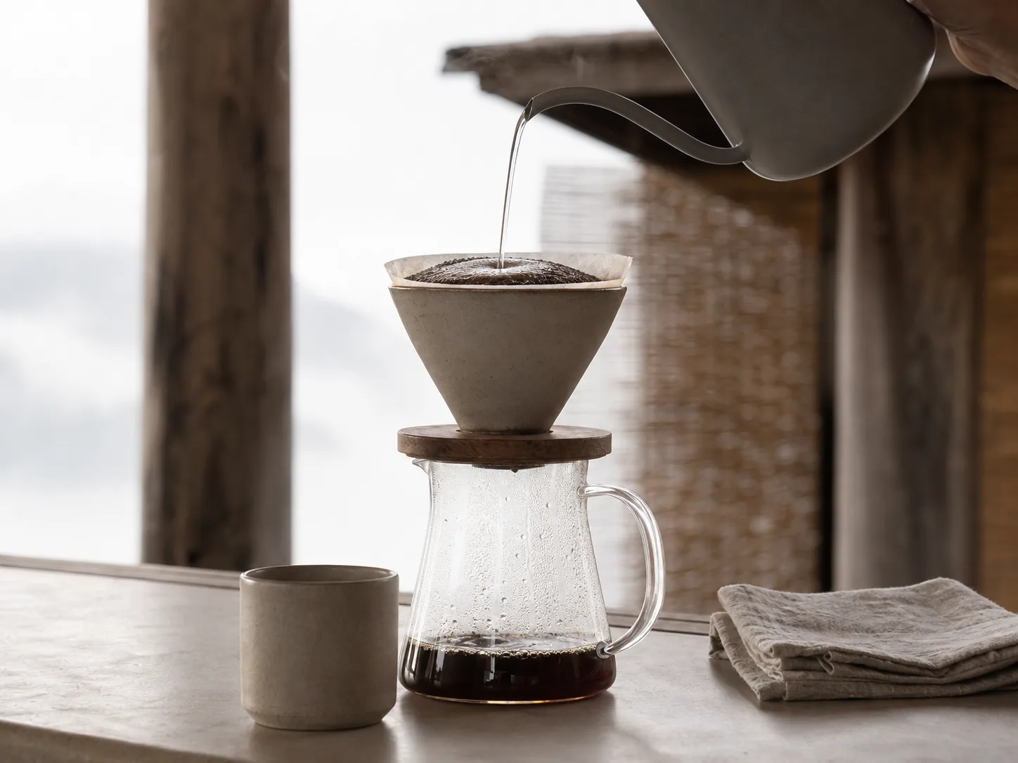 A pour-over cone mid-brew, bloom rising, seen close from the side